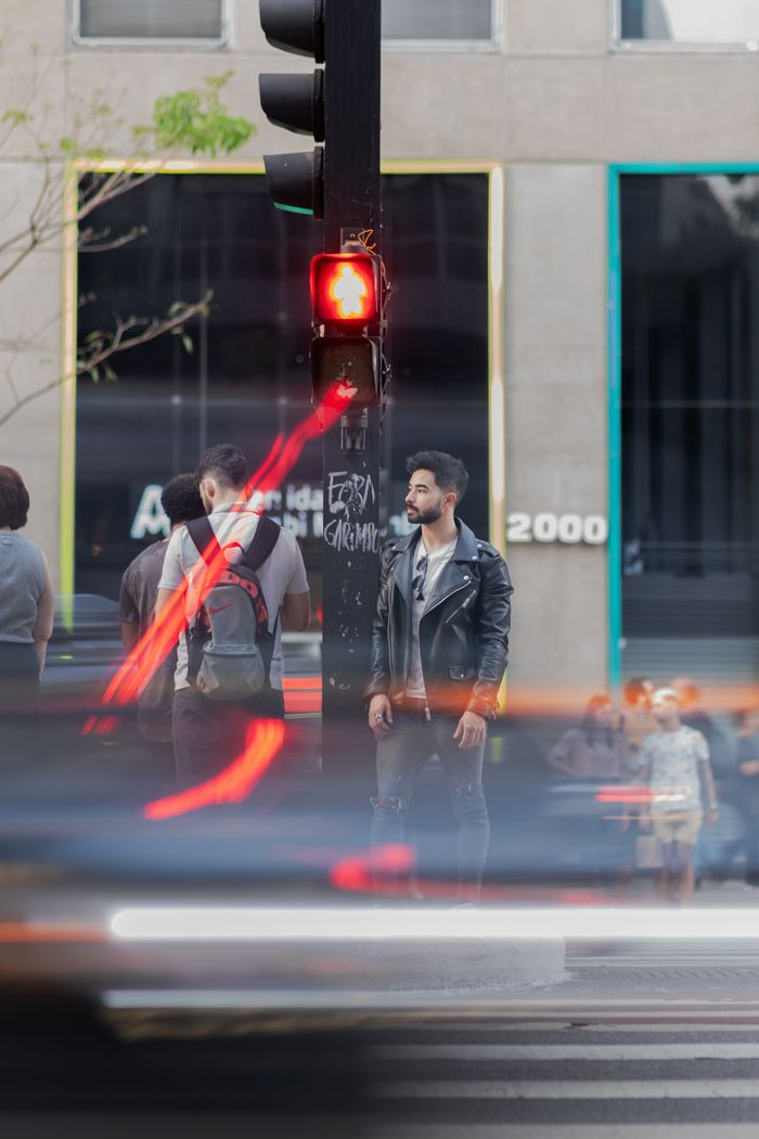 gallery-6 Dynamic city street scene with motion blur, featuring fashionably dressed man at crosswalk.