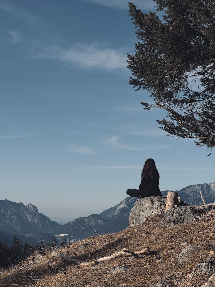 why-choose-us Woman meditating on a mountain overlooking scenic landscapes and forests.