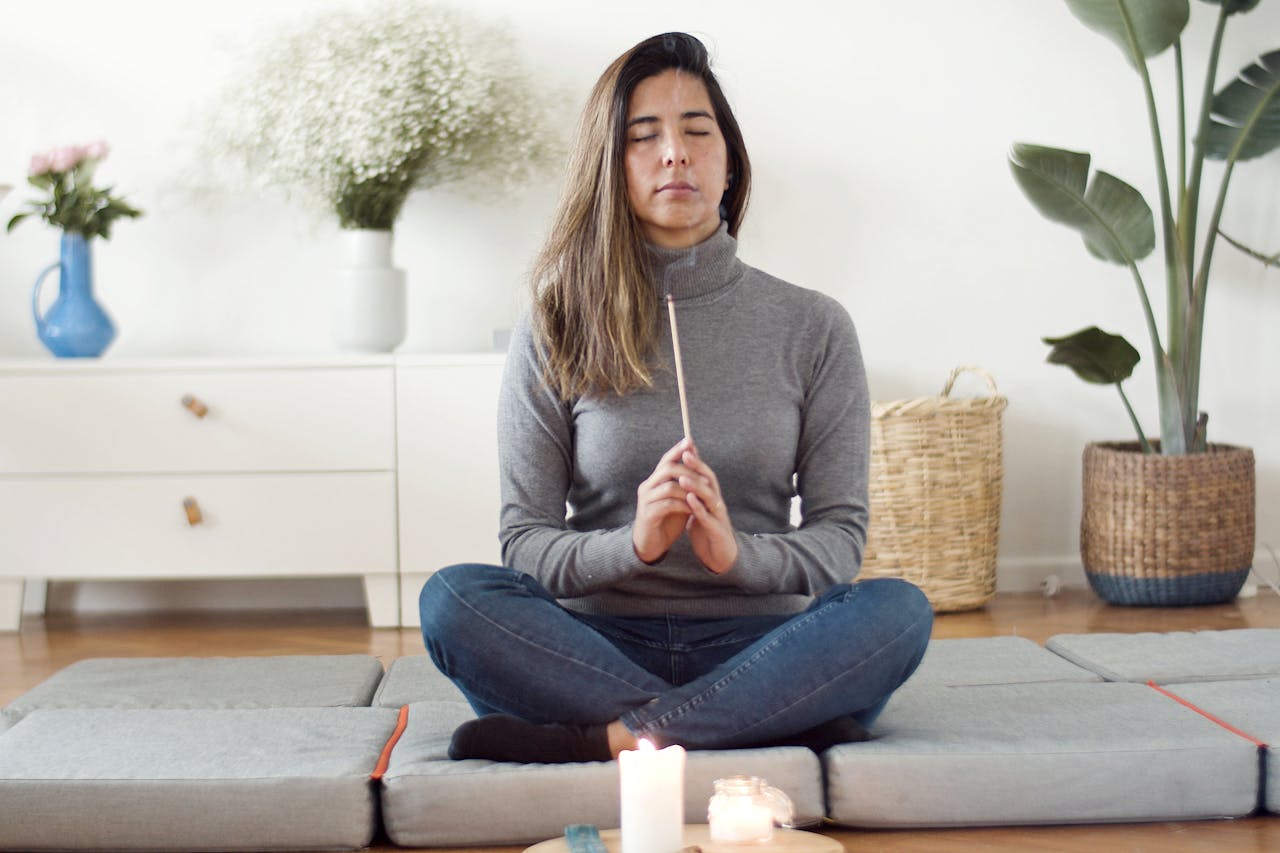 services-03 A woman practicing mindfulness meditation indoors, holding incense.
