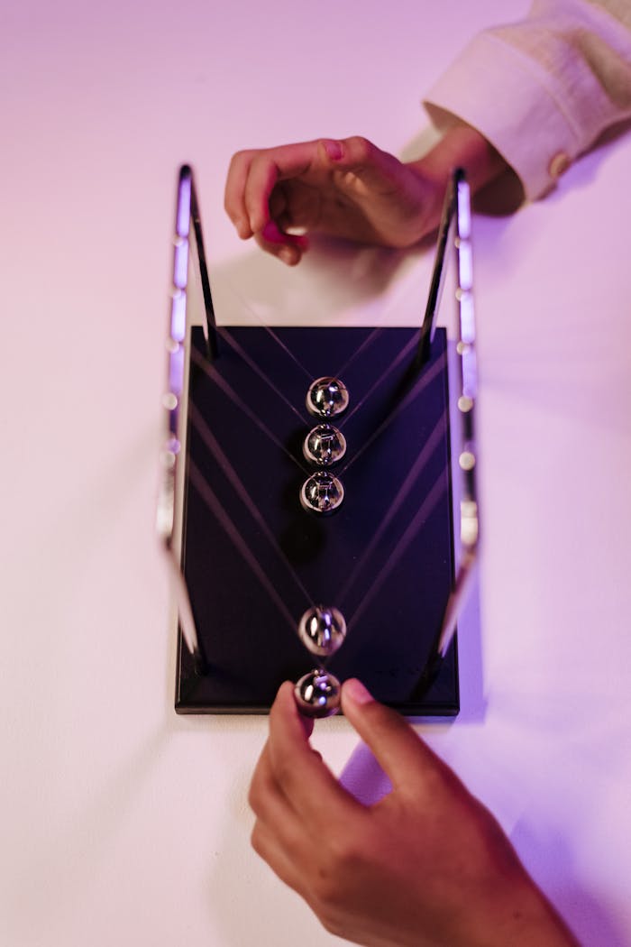 gallery-5 A close-up view of a Newton's cradle being activated by hands showcasing physics in motion.